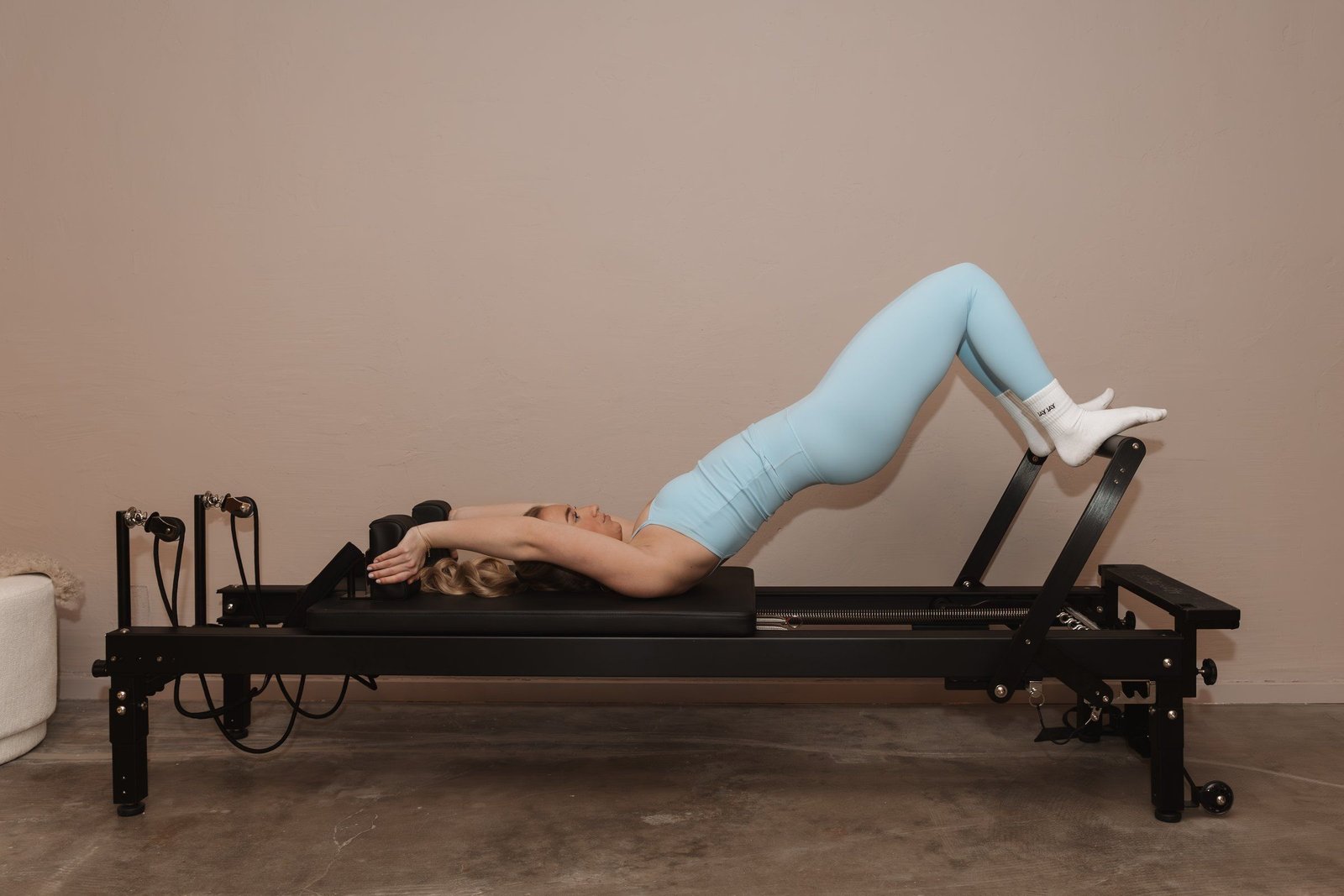 Een vrouw maakt een brug op de reformer, tegen de lichte wand van de studio